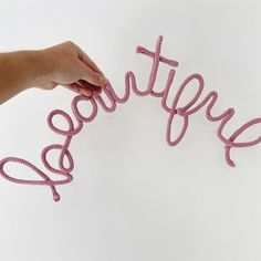 a hand is holding string that spell out the word happy on a white surface with pink beads