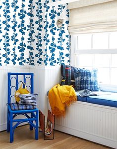 a blue chair sitting in front of a window next to a white wall with flowers on it