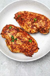 two chicken patties on a white plate with green garnish and parsley