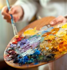 a person holding a paintbrush in their hand and painting on an art easel