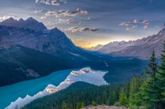 the sun is setting over a mountain lake in the canadian rockies, with pine trees surrounding it