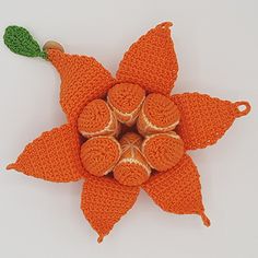 an orange crocheted flower with green leaves on it's end and four balls in the center