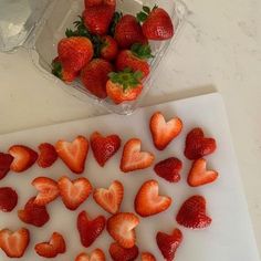 strawberries are arranged in the shape of hearts on a cutting board next to a container of water