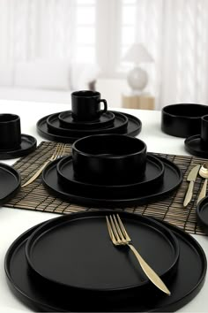 a table set with black plates and goldware