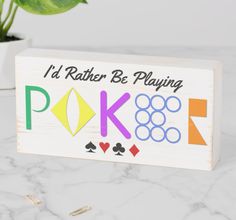 a wooden sign that says i'd rather be playing poker on the table next to a potted plant