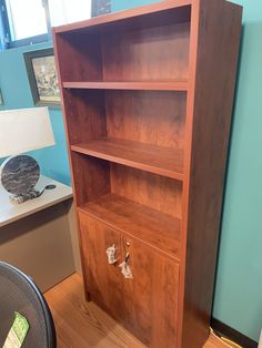 a wooden bookcase sitting on top of a hard wood floor next to a lamp