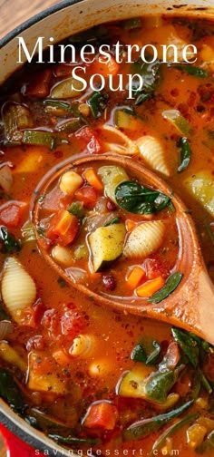 a red pot filled with minestone soup on top of a wooden table next to a spoon