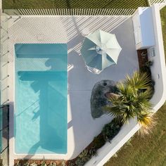 an aerial view of a pool and umbrellas in a backyard with grass, shrubs and trees