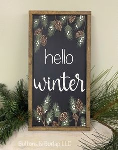 a sign that says hello winter with pine cones and evergreen leaves on it next to some branches