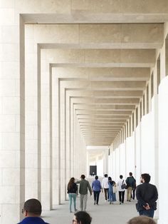 several people walking down a long hallway lined with white pillars and columns on either side