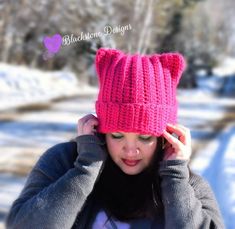 a woman wearing a pink knitted hat while holding her hands to her head in the snow