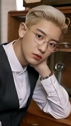 a young man wearing glasses sitting at a desk with his hand on his chin and looking off to the side