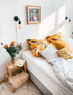 a white bed topped with lots of pillows next to a wooden end table and lamp