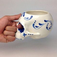 a hand holding a white and blue skull mug