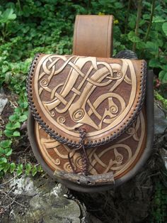 a brown leather backpack sitting on top of a rock in front of some trees and bushes