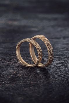 two gold wedding rings sitting on top of a black surface with one ring in the middle