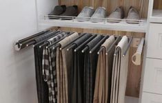 an organized closet with shoes and pants hanging on the wall, along with white drawers