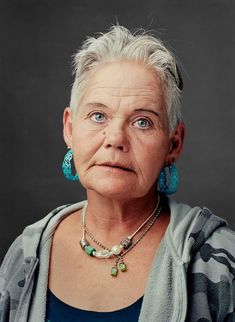 an older woman with grey hair wearing blue earrings and a gray cardigan sweater is looking at the camera