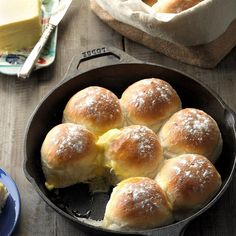 a pan filled with rolls covered in powdered sugar on top of a wooden table