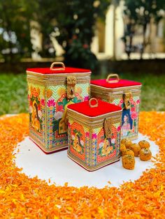 three colorful boxes sitting on top of a table covered in orange flowers and grass next to each other