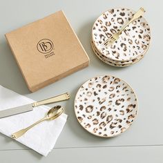 the leopard print plates are next to goldware and a box with utensils