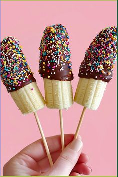 three chocolate covered banana pops with sprinkles on them in front of a pink background