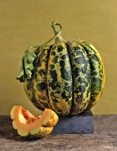 two melons sitting on top of a wooden table next to a piece of fruit