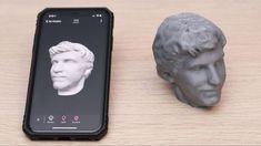 a cell phone sitting next to a statue of a man's head on top of a wooden table