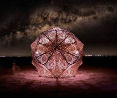 a large light sculpture sitting on top of a sandy beach under a night sky filled with stars