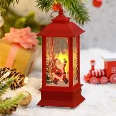 a red lantern sitting on top of a snow covered ground next to a christmas tree