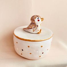 a small ceramic bird sitting on top of a white container with polka dot trimmings