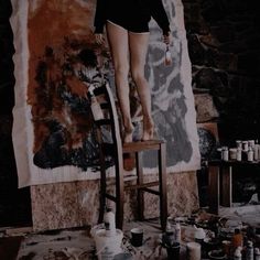 a woman standing on top of a wooden chair in front of a wall covered with paint