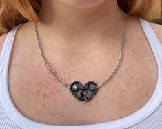 a woman with red hair wearing a white tank top and silver chain necklace that has two black hearts attached to it