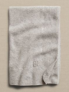 the back of a gray sweater folded on top of a white surface with an embroidered b logo