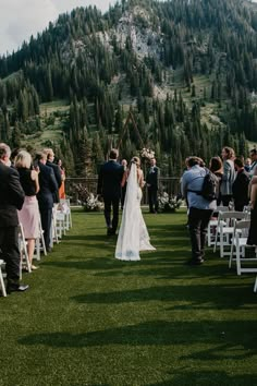 a bride and groom walking down the aisle at their wedding ceremony in front of a mountain