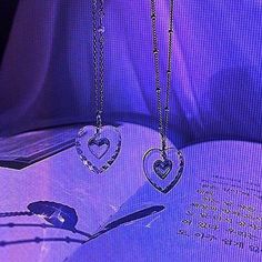 two heart - shaped pendants are hanging from a book on a purple light background