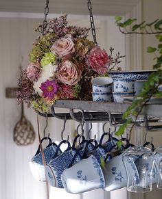 tea cups and saucers are hanging from a rack with flowers in the background,