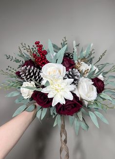 a bridal bouquet with red and white flowers, pineconis, berries and greenery