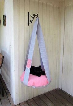 a black cat laying on top of a pink cushion in a hammock hanging from a hook