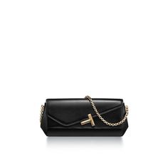 Inspiring, empowering and above all, unwavering, the Tiffany T collection reminds us of the connections we feel but cannot always see. This Tiffany T clutch is crafted in shiny calf leather with gold-plated brass hardware. It features a slip pocket, a small mirror pocket, a T square chain and a Tiffany T logo on the front. Black shiny calf leather; Gold-plated brass hardware; One slip pocket and one small mirror pocket; Magnet closure; 5.1" H x 11.4" L x 2.2" W; Chain is 21.7" long | Tiffany T C Tiffany T, T Logo, Small Mirrors, Gold Chain Necklace, Gift List, Gold Pendant Necklace, Brass Hardware, Chains Necklace, Gold Chains