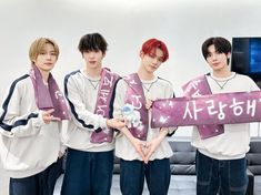 four young men holding up signs in front of a television screen with korean characters on them