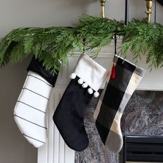 two stockings hanging from a mantel decorated with evergreen branches and pom - poms