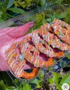 a person holding up several donuts with sprinkles on them in front of some trees