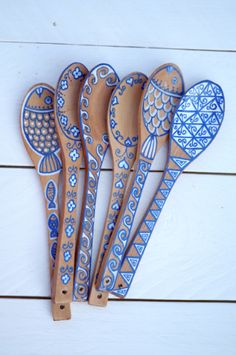 six wooden spoons with designs on them are lined up against a white wood background