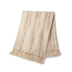 a beige knitted blanket with fringes on the bottom and sides, against a white background