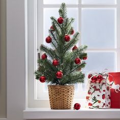 a small christmas tree in a basket next to a window sill with presents on the windowsill