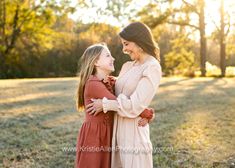 two women standing in the grass with their arms around each other and looking at each other