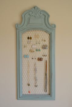 a blue frame with jewelry hanging from it's sides on the wall next to a white wall