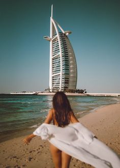 a woman is walking on the beach in front of a tall burj building