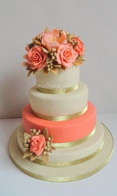 a three tiered cake with pink and gold flowers on the top, sitting on a white table